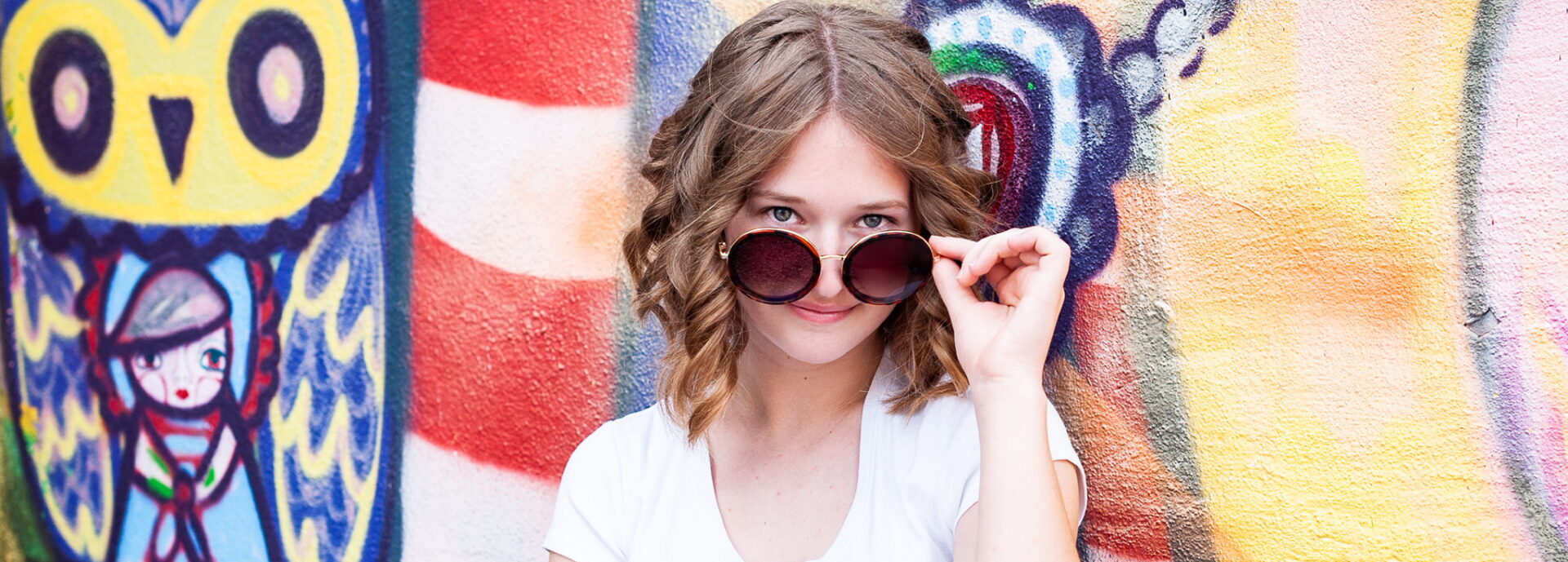 Abby in sunglasses in front of a colorful mural